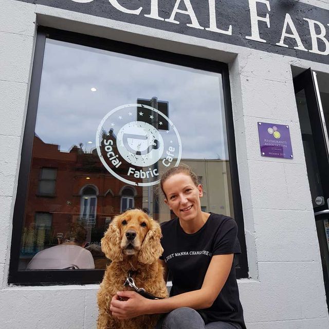 A staff member with a dog outside a Social Fabric Café 